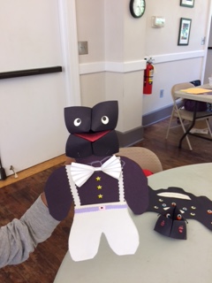 Paper person puppet with a tuxedo made from construction paper, including a bow tie from folded paper